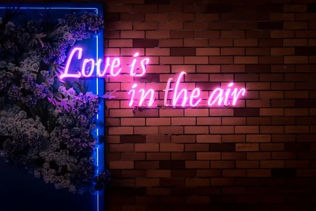 a brick wall with greenery and a pink neon sign that reads love is in the air for neon pink aesthetic