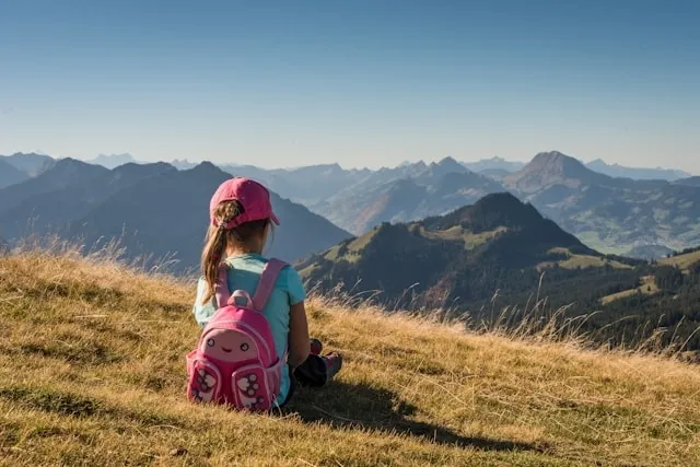 a child wearing a pink backpack while sitting and looking at a mountainous landscape for how to organize your backpack