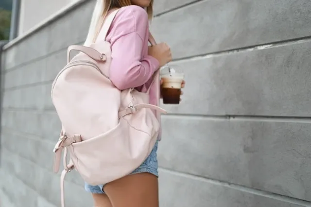 a woman carrying a pink backpack while holding a cup of coffee for how to organize your backpack