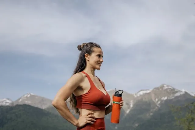 a woman in red workout gear holding a tumbler in front of a mountainous landscape for tumbler ideas for ladies