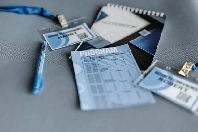 printout paper, spiral notebook, pen, and badges on a gray surface for trade show planning printout paper, spiral notebook, pen, and badges on a gray surface for trade show planning
