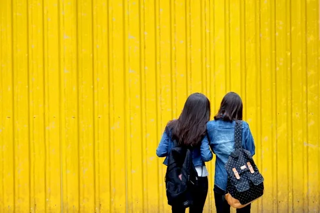 two women carrying backpacks in front of a yellow wall for when were backpacks invented two women carrying backpacks in front of a yellow wall for when were backpacks invented