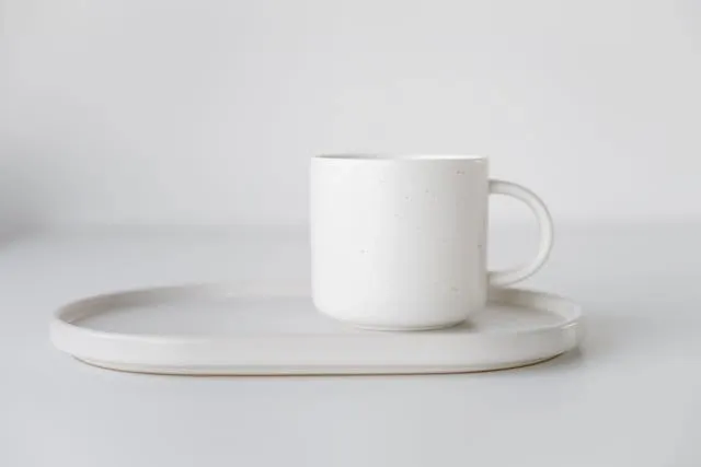 a white mug on a white plate against a white background for porcelain vs ceramic mugs