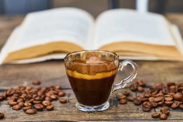 a clear glass mug with a coffee beverage beside a book for best glass coffee mugs