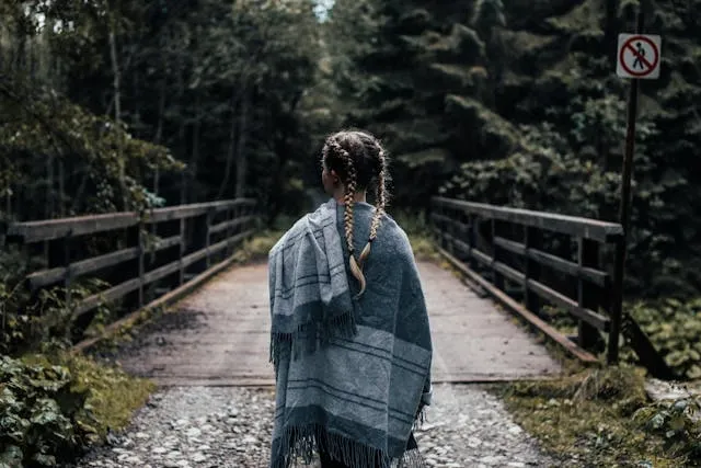 a person in a gray shawl standing on a forest bridge for different fringes for scarves