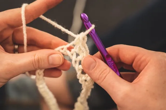 hands using a purple crochet hook with white yarn
