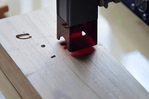 Laser engraving machine burning a design into a light wood coaster blank