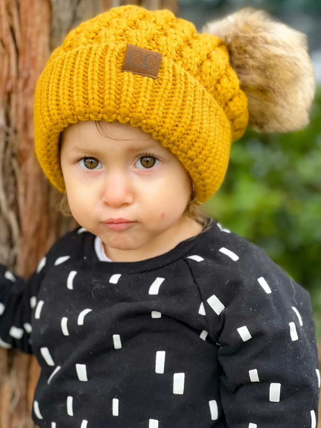 Toddler fiercely looking at camera with a beautiful yellow beanie with puffy ears