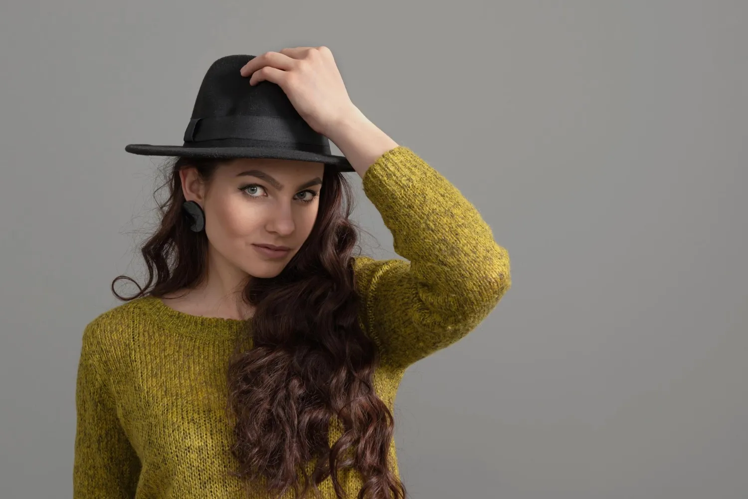 Close-up portrait of a beautiful and positive young girl in a black hat isolated on gray background