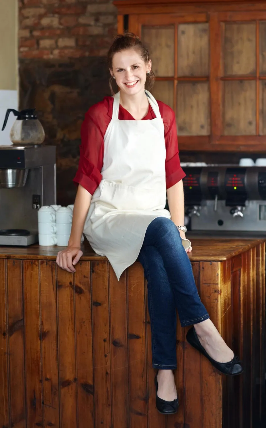 Woman in portrait barista at coffee shop and sit on countertop happy employee in hospitality industry female professional in cafe small business owner and entrepreneur smile with positive mindset