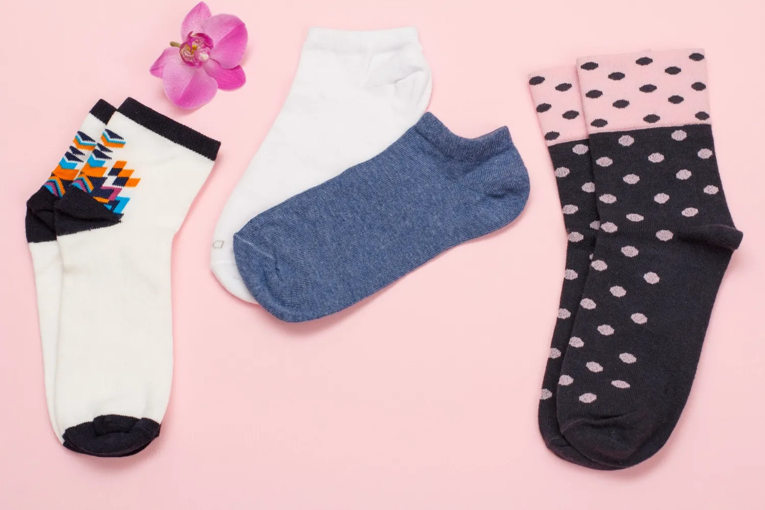 Color pairs of women socks and orchid flower on pink background, top view.