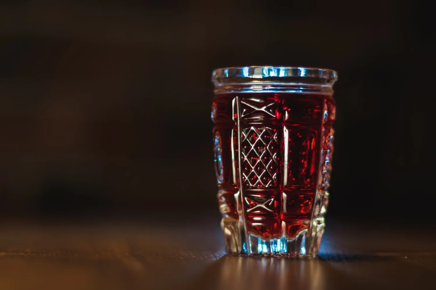 Tincture of red color in a crystal glass stands on a wooden table