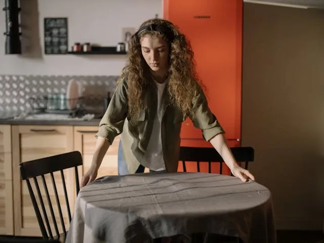 a woman putting a tablecloth on a small round table for types of tablecloth