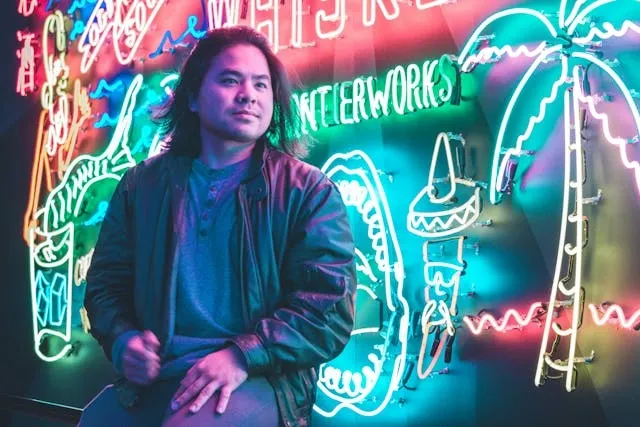 a man sitting by a neon light display for neon sign repair cost