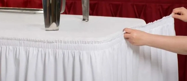 someone applying a table skirt to a table for how to attach table skirt without clips