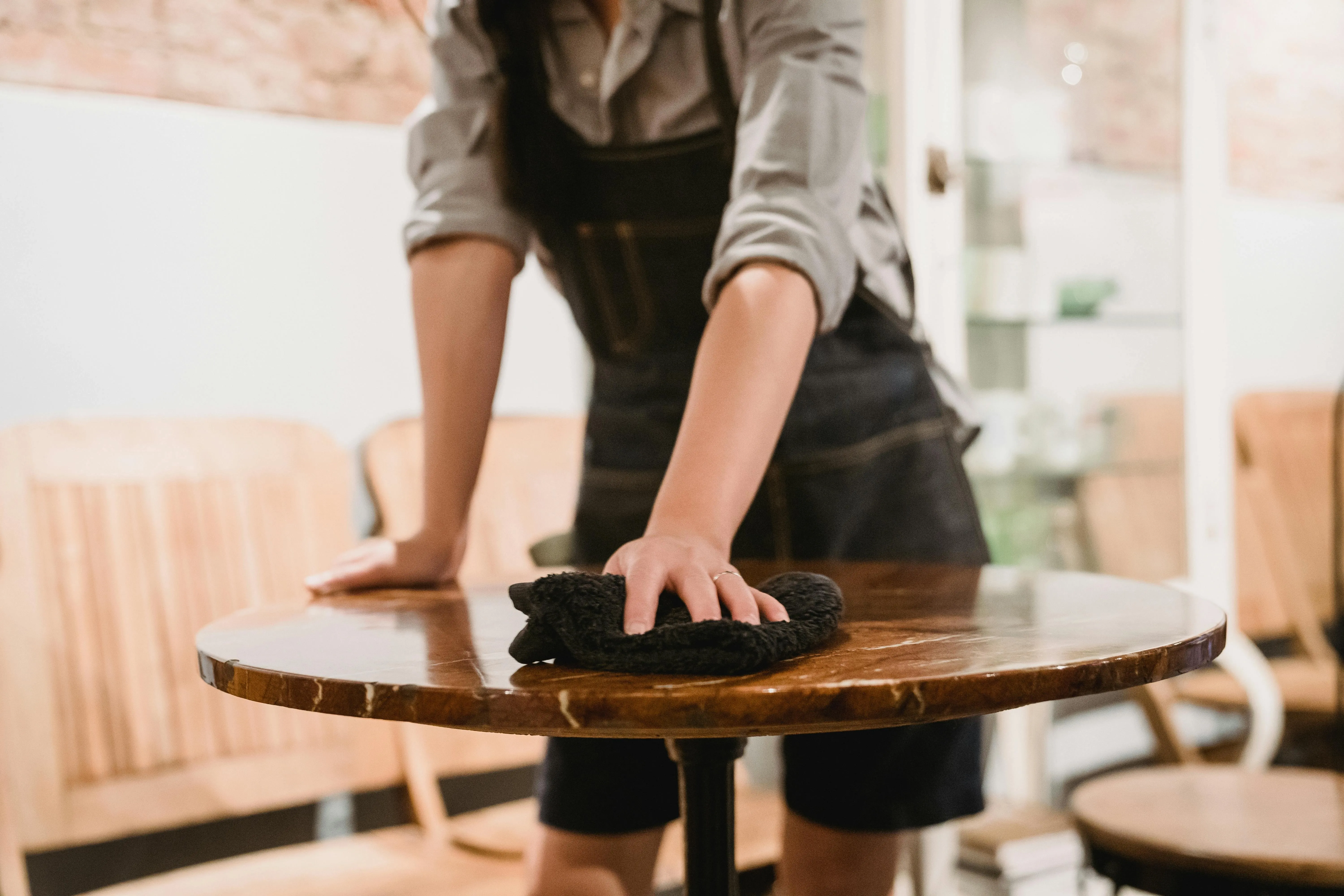 someone cleaning a wooden table in a cafe for how to clean a wood table that is sticky