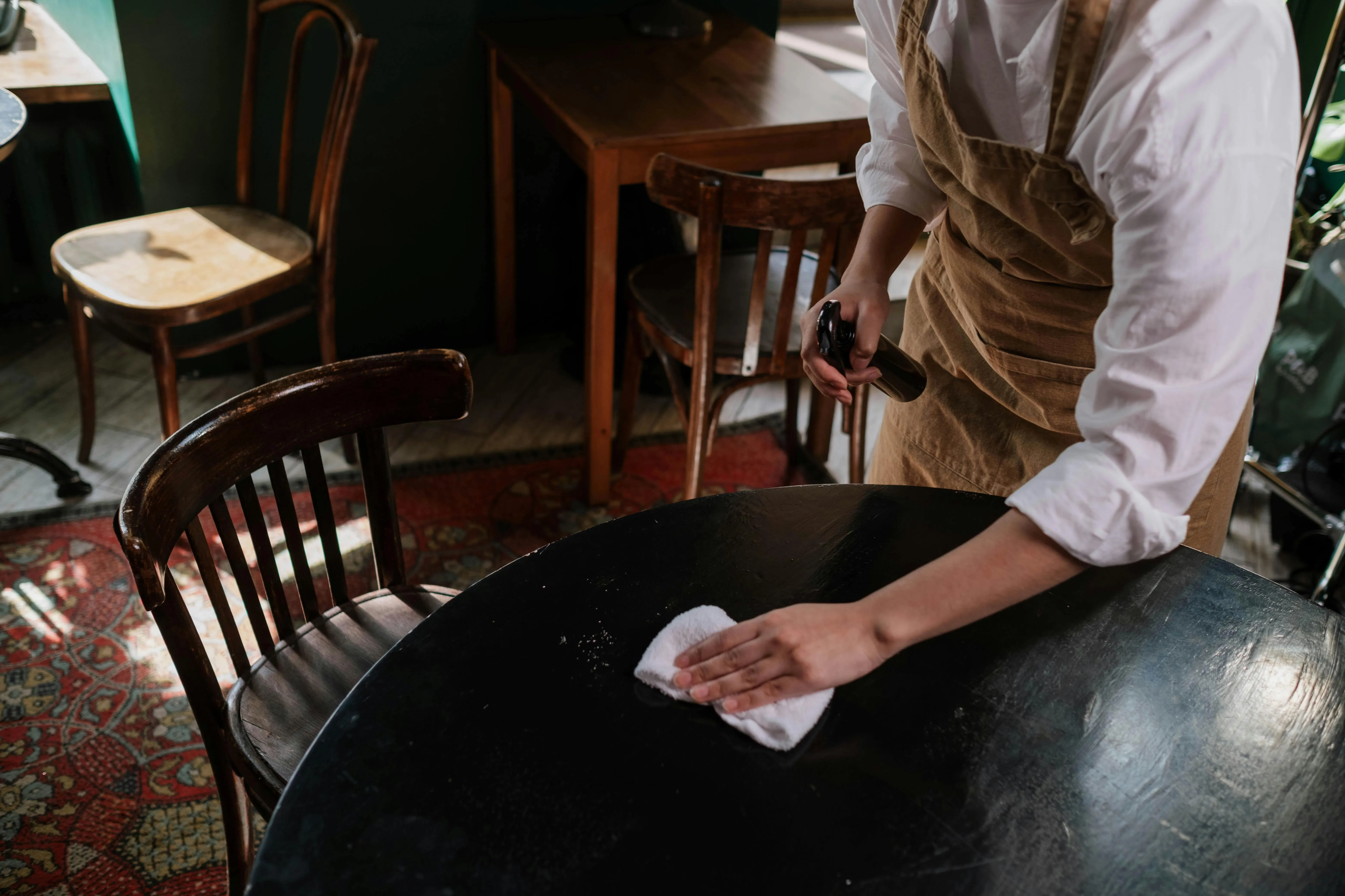 someone wiping down a table in a restaurant for how to clean tables in a restaurant