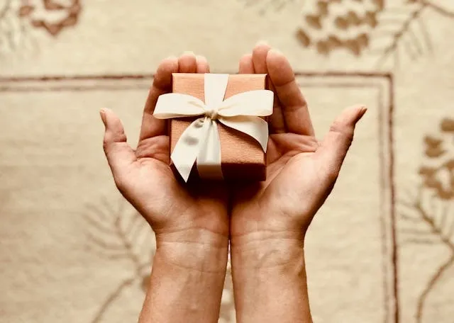 two hands holding a small giftwrapped box for employee appreciation gifts