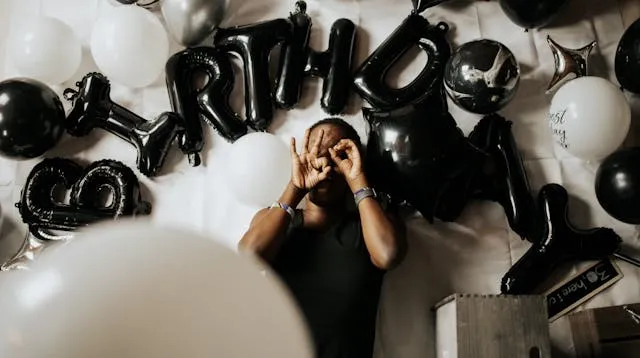 a person sitting amid a display of balloons that says birthday for birthday party checklist for adults