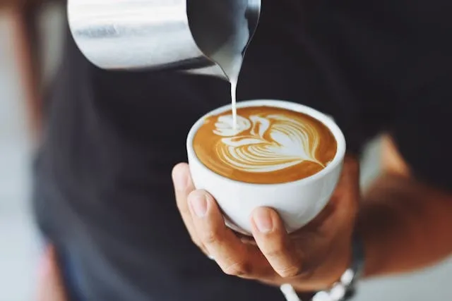 a person pouring milk into a cup of coffee for coffee bar ideas for small spaces