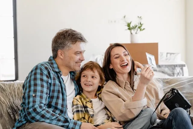 a happy couple with a child smiling as they look at a photograph for housewarming gifts for couples