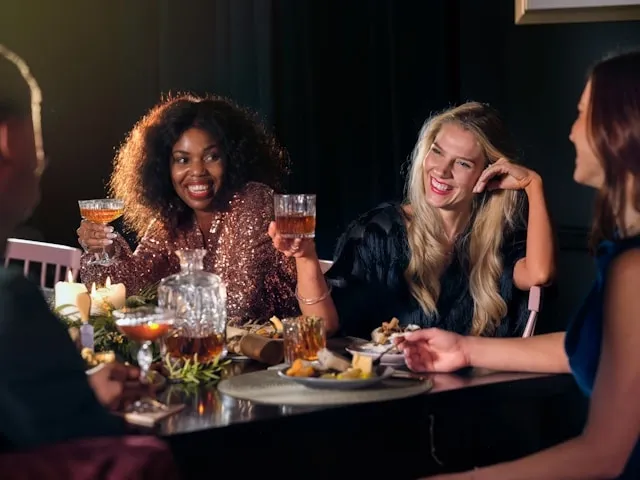 people sitting around a table with food and drinks for dinner party essentials