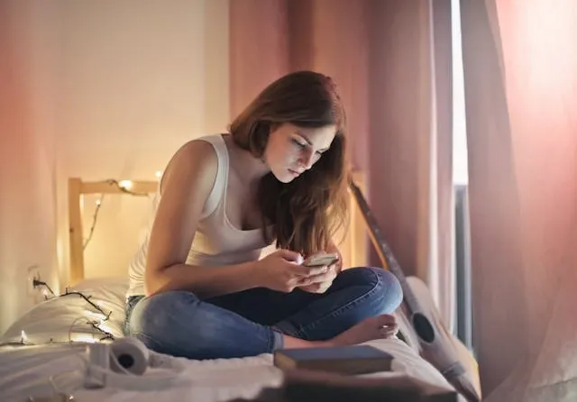 a woman sitting on a bed surrounded by fairy lights and pink curtains for girl aesthetic room ideas