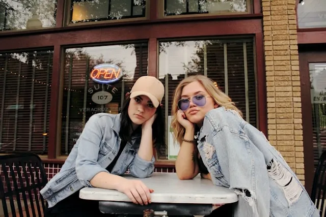 two people wearing jean jackets sitting outside a cafe for how to style a jean jacket