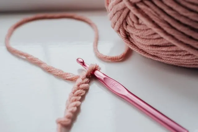 some pink yarn and a crochet needle for crochet coasters