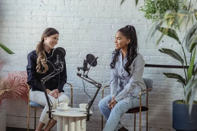 two women having a conversation with microphones in front of a white wall for podcast room ideas