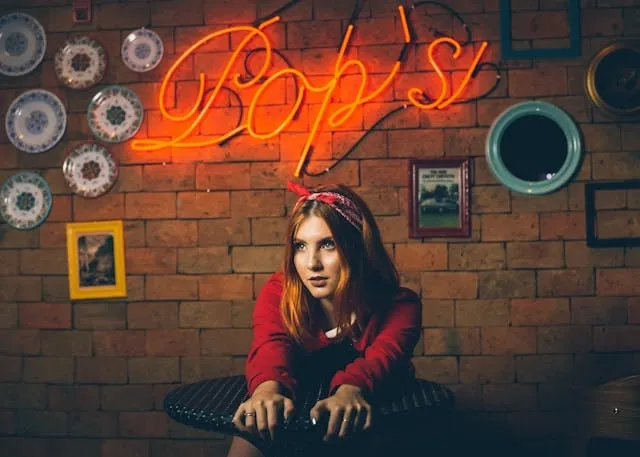 a woman sitting at a table below a red neon sign on an exposed brick wall for restaurant decor ideas