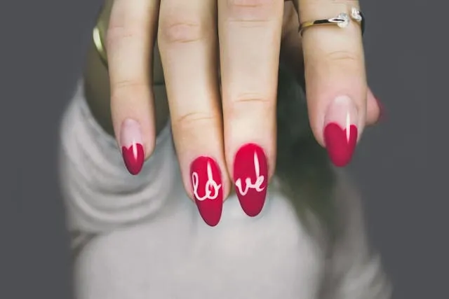 nails painted in vibrant red with the word love written for nail salon design