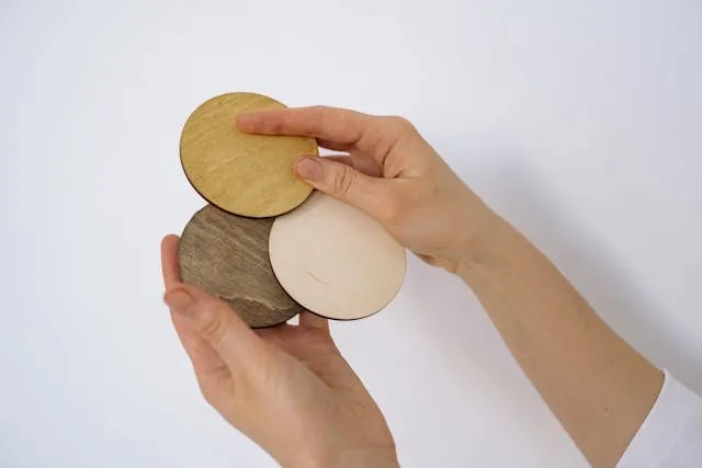 a person’s hands holding three round wooden coasters for best finish for wood coasters