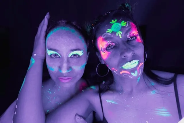 two women wearing uv face paint under a black light for neon theme party