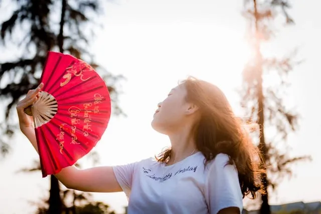 a woman using a red hand fan for can you bring a fan on a plane