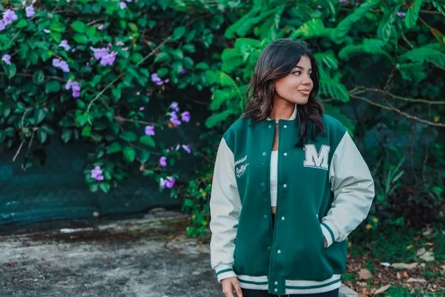 a woman standing outdoors wearing a green letterman jacket with an m patch for how to make chenille patches