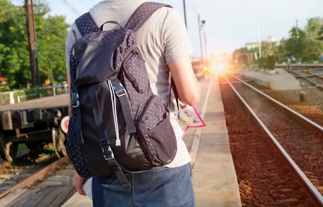 a person with a backpack waiting at a train station for can you put a backpack in the washer